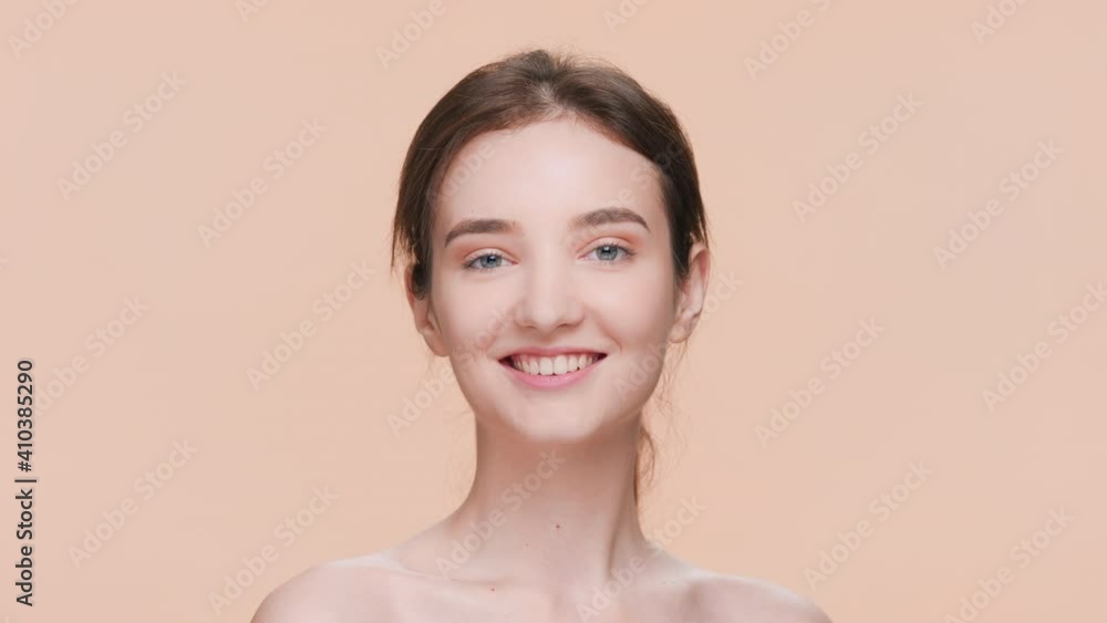 Young attractive brunette woman with a perfect skin looks up at the camera and smiles against a dark beige background | Skin care product advertising concept Young attractive brunette woman with a perfect skin looks up at the camera and smiles against a dark beige background | Skin care product advertising concept