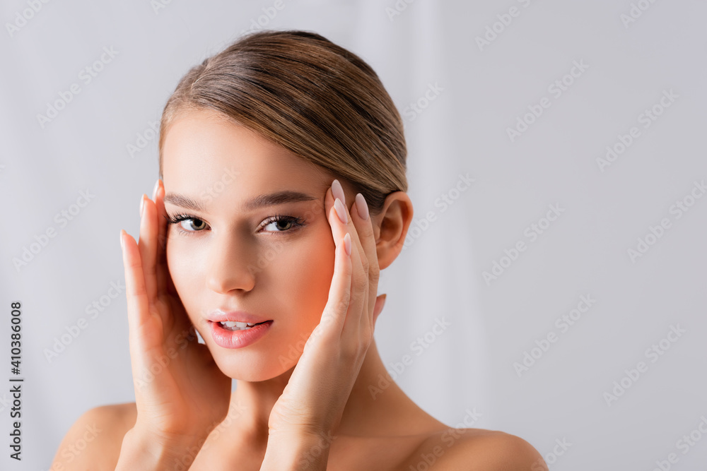 young woman with bare shoulders looking at camera and touching face on white young woman with bare shoulders looking at camera and touching face on white