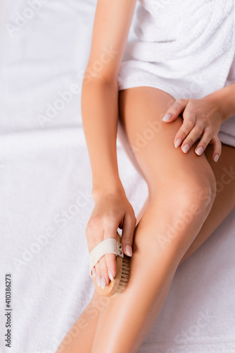 cropped view of woman wrapped in white towel exfoliating skin on leg