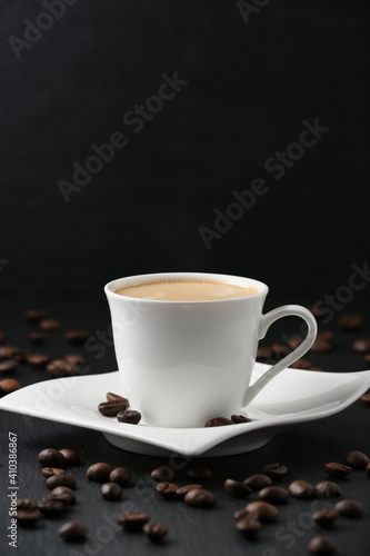 White cup of coffee on a black background. Close-up side view. Vertical photography. Coffee beans on a black table.