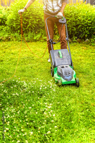 Man cutting green grass with lawn mower in backyard. Gardening country lifestyle background. Beautiful view on fresh green grass lawn in sunlight, garden landscape in spring or summer season.