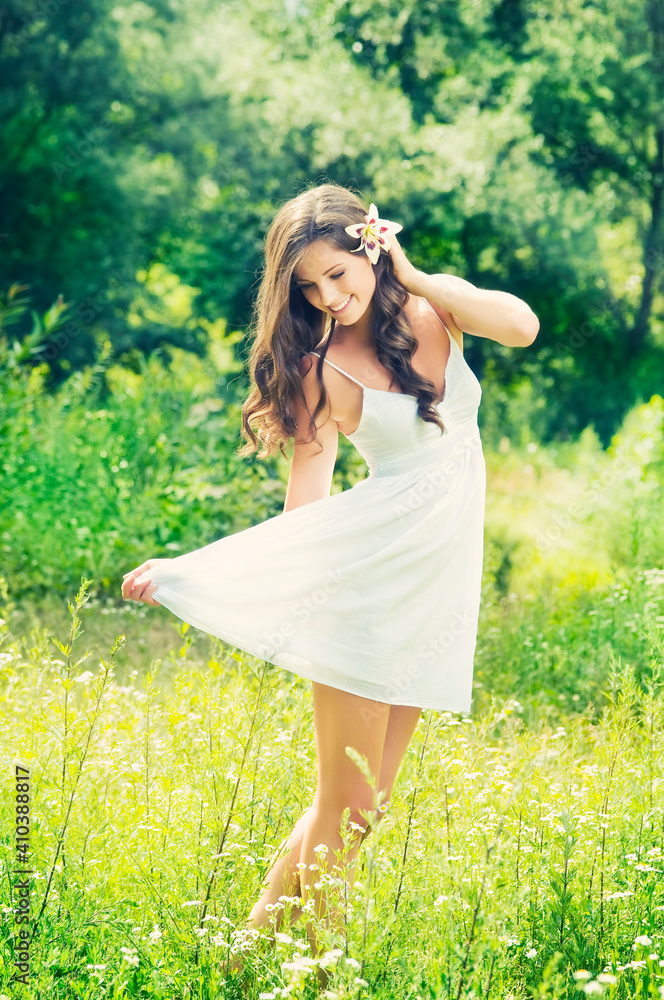 Smiling young woman in white dress with flower against background of summer green park. Beautiful healthy happy girl enjoying freedom outside in nature. Smiling young woman in white dress with flower against background of summer green park. Beautiful healthy happy girl enjoying freedom outside in nature.