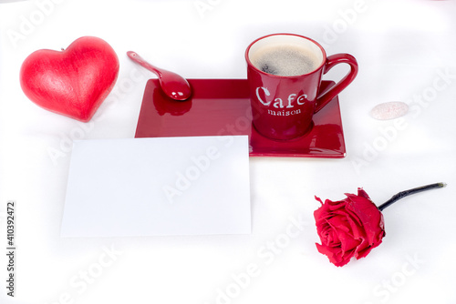 Red coffee cup with a white and blank gift card placed in front, surrounded by a red love heart and a red rose., white background. Love and valentine's day 