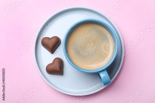 Romantic breakfast with cup of coffee and chocolate candies on pink background, top view. Valentine's day celebration