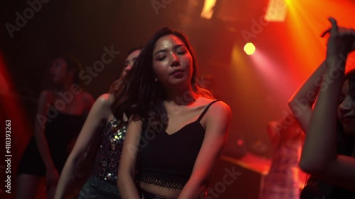 Group of Asian woman friend dancing to dj club music with multi-color illuminated neon night lights at night club. Fashionable female enjoy and having fun with nightlife dance party at disco nightclub