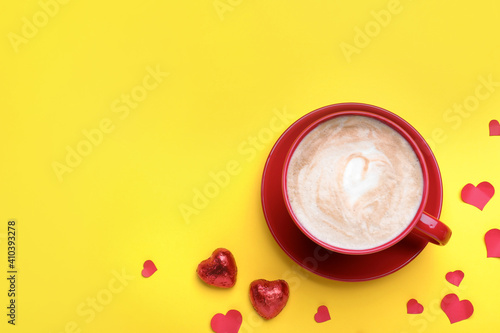 Cup of coffee, chocolate candies and paper hearts on yellow background, flat lay with space for text. Valentine's day breakfast