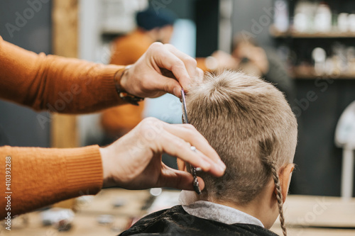 the process of cutting a blond boy with a long braid in a chair in a barbershop salon, a barbershop concept for men and boys