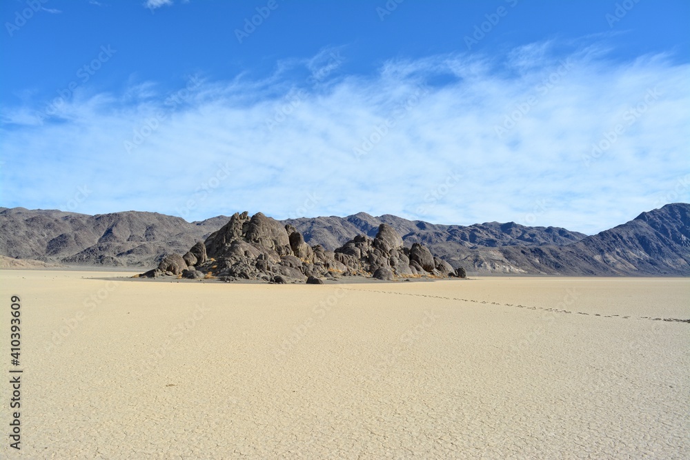 The Grandstand on the Racetrack Playa in the Death Valley National Park, a very dark grey rock surrounded by featureless, light tan-colored clay sediment in a dry lake bed
