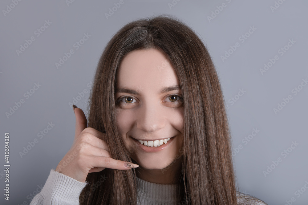 Portrait of funny adorable young lady woman girl wear sweater showing us a call me sign phone asking call her back isolated gray color background