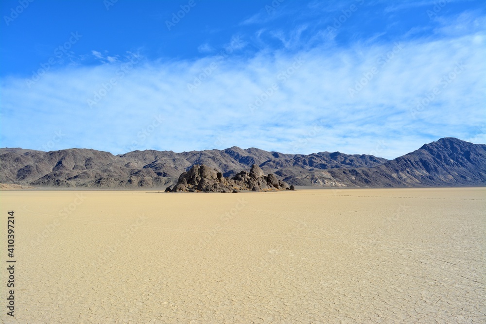 The Grandstand on the Racetrack Playa in the Death Valley National Park, a very dark grey rock surrounded by featureless, light tan-colored clay sediment in a dry lake bed