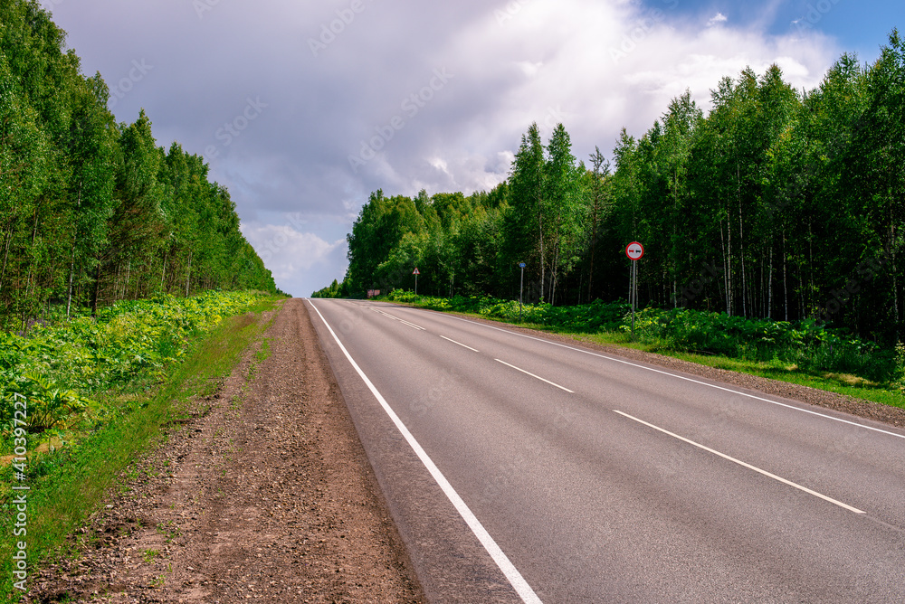 An asphalted intercity road with white markings extending into the distance through a green forest.