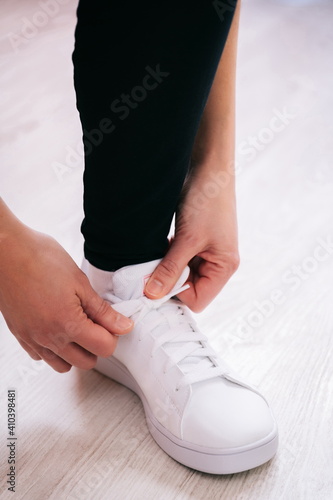 Sportsman tying white sneaker on light background