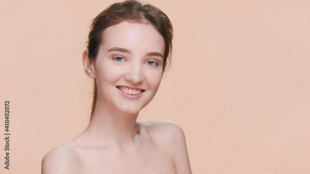 Young brown-haired beauty model gently touches her shoulder, sliding her hand down her arm, turns and looks at the camera and smiles | Posing for skin care product commercial Young brown-haired beauty model gently touches her shoulder, sliding her hand down her arm, turns and looks at the camera and smiles | Posing for skin care product commercial