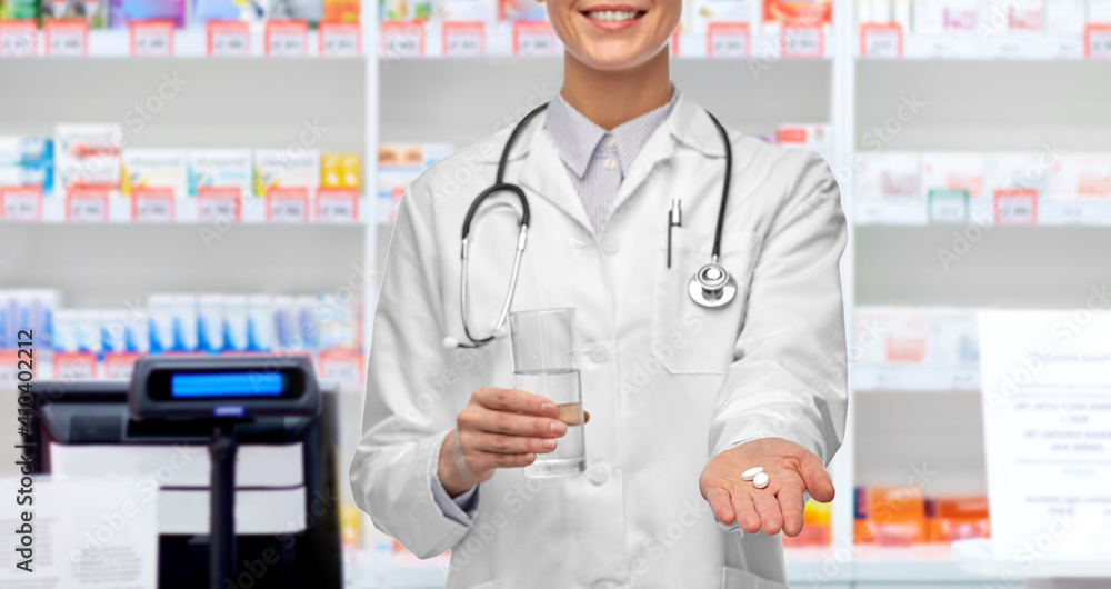 medicine, profession and healthcare concept - close up of happy smiling female doctor or pharmacist with pill and glass of water over pharmacy background
