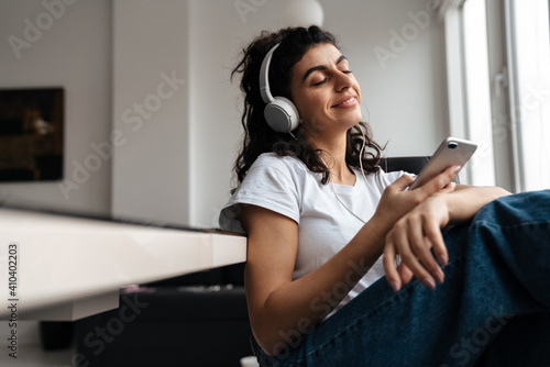 Happy relaxed woman in headphones using mobile phone while sitting