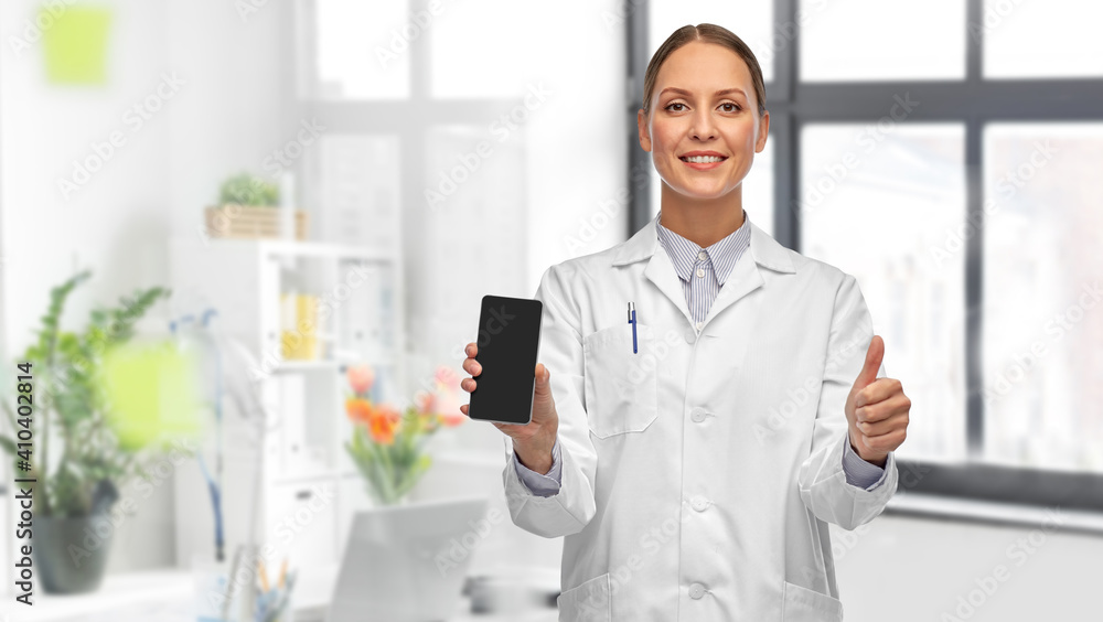 medicine, profession and healthcare concept - happy smiling female doctor showing smartphone and thumbs up over medical office at hospital on background