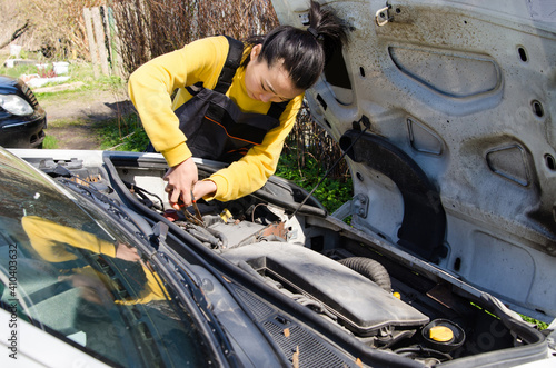 Asian female mechanic dressed in special clothes fixing a car near the house