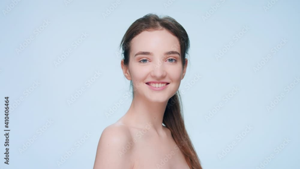 Young fresh-looking positive brunette woman with a ponytail turns to the camera and smiles against a blue seamless background | Skin care and beauty care product commercial concept Young fresh-looking positive brunette woman with a ponytail turns to the camera and smiles against a blue seamless background | Skin care and beauty care product commercial concept