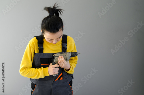 Asian Female construction worker dressed in special clothes with a cordless screwgun, a construction tool isolated on grey background photo