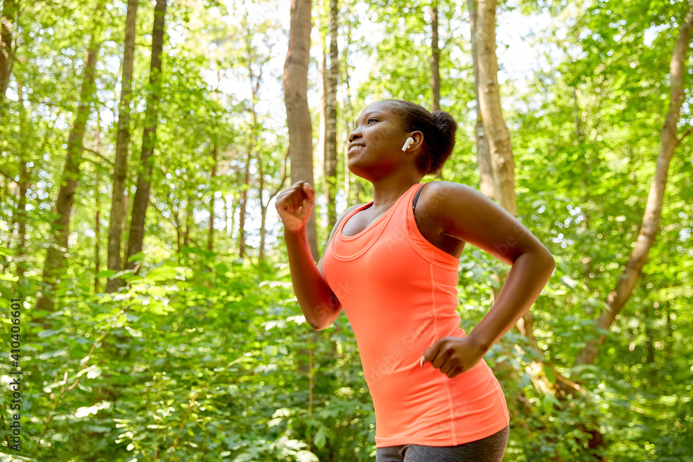 fitness, sport and healthy lifestyle concept - happy smiling young african american woman with earphones running in park fitness, sport and healthy lifestyle concept - happy smiling young african american woman with earphones running in park