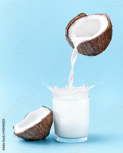 Cracked coconut with splashes of milk on blue background. coconut milk is poured into the glass