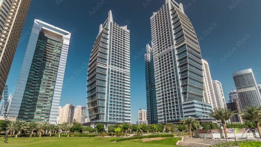 Timelapse hyperlapse view on skyscrapers at waterfront with palms. Residential buildings covered with glass in Jumeirah Lake Towers near park in Dubai, UAE. View from park Timelapse hyperlapse view on skyscrapers at waterfront with palms. Residential buildings covered with glass in Jumeirah Lake Towers near park in Dubai, UAE. View from park