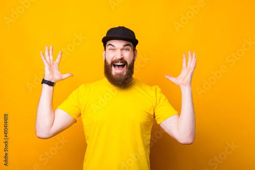 Portrait of young bearded hipster man making surprised gesture over yellow background.