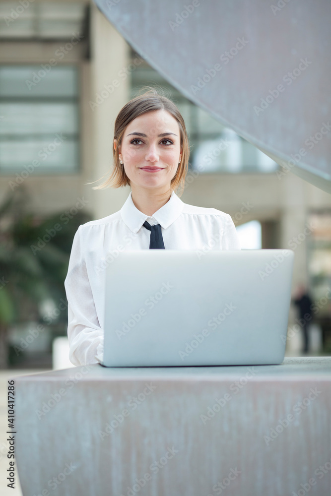 manager donna bionda con i capelli a caschetto, camicia bianca e cravatta nera, lavora al computer in esterni e sorride felice manager donna bionda con i capelli a caschetto, camicia bianca e cravatta nera, lavora al computer in esterni e sorride felice