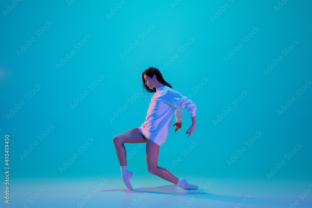 Stylish. Young and graceful ballet dancer isolated on blue studio background in neon light. Art, motion, action, flexibility, inspiration concept. Flexible caucasian ballet dancer, soft moving.
