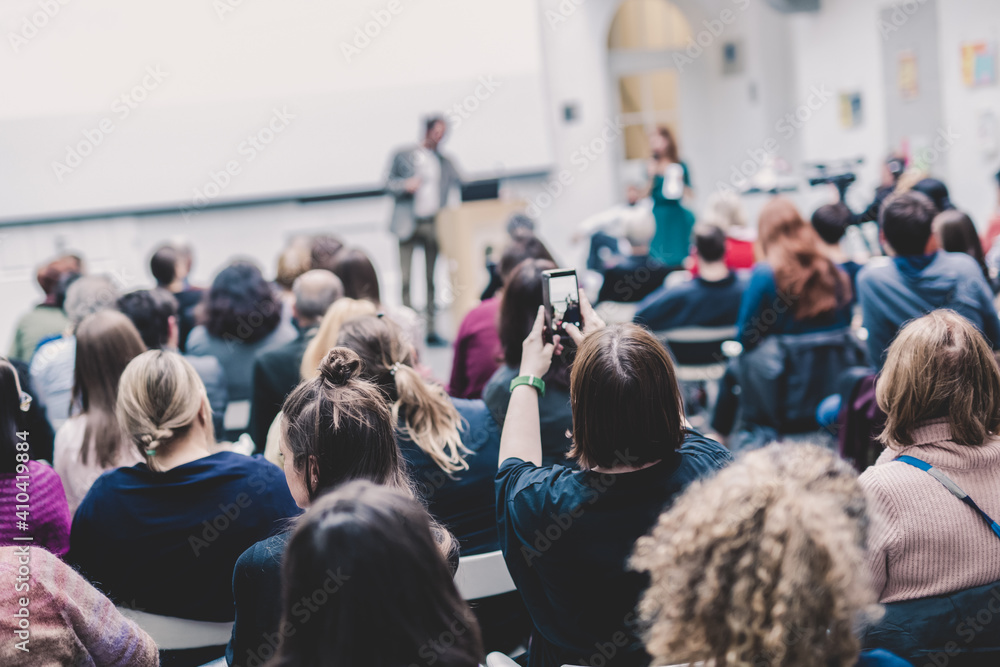 Obraz premium Male speaker giving presentation in lecture hall at university workshop. Audience in conference hall. Rear view of unrecognized participant in audience. Scientific conference event.