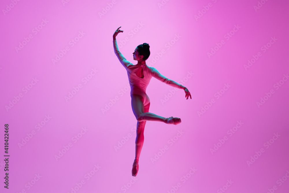 Beautiful. Young and graceful ballet dancer on pink studio background in neon light. Art, motion, action, flexibility, inspiration concept. Flexible caucasian ballet dancer, moves in glow.