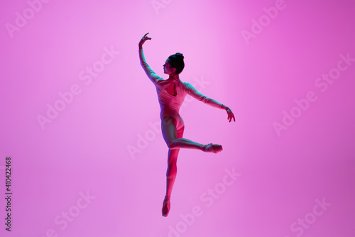 Beautiful. Young and graceful ballet dancer on pink studio background in neon light. Art, motion, action, flexibility, inspiration concept. Flexible caucasian ballet dancer, moves in glow. © master1305