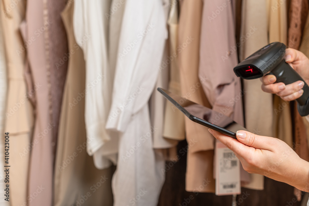 Female entrepreneur holding tablet, barcode scanner while doing inventory in her trendy clothing shop