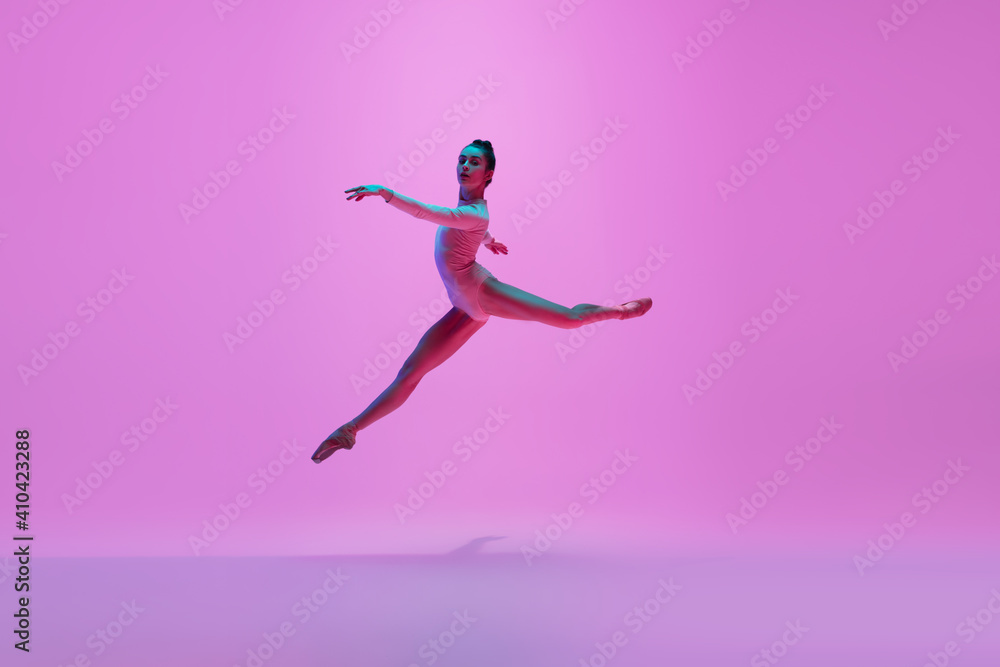 Beautiful. Young and graceful ballet dancer on pink studio background in neon light. Art, motion, action, flexibility, inspiration concept. Flexible caucasian ballet dancer, moves in glow.