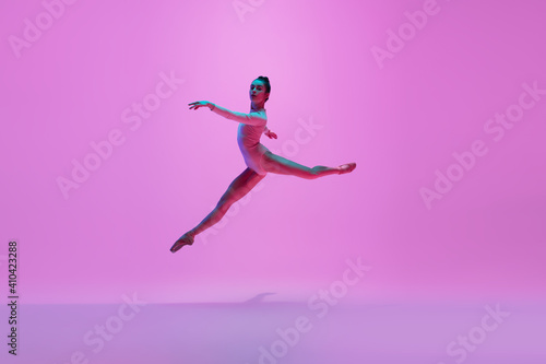 Beautiful. Young and graceful ballet dancer on pink studio background in neon light. Art, motion, action, flexibility, inspiration concept. Flexible caucasian ballet dancer, moves in glow. © master1305