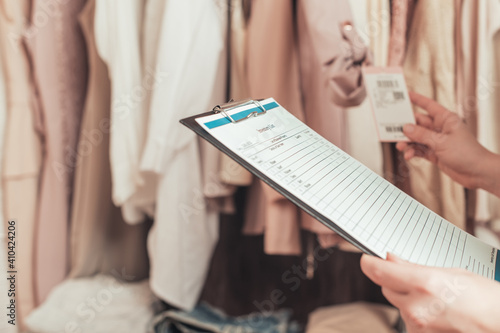 Female entrepreneur holding a clipboard with inventory list while doing inventory in her trendy clothing shop