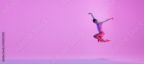 Young and graceful ballet dancer isolated on pink studio background in neon light. Art, motion, action, flexibility, inspiration concept. Flexible caucasian ballet dancer, moves in glow. Flyer