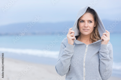 Bellissima ragazza bionda con abbigliamento sportivo, si rilassa in riva al mare tenendosi il cappuccio. photo
