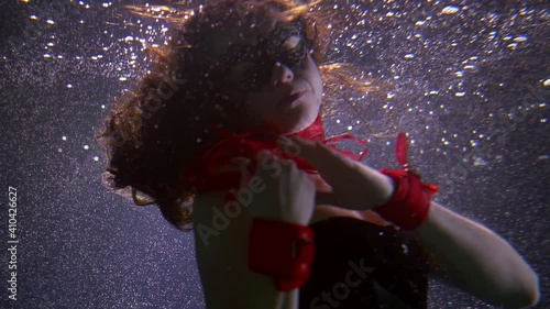 sexual woman is wearing mysterious mask and corset is swimming underwater, stroking her body by knout photo