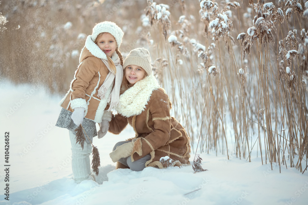 Obraz premium Family walk in winter park Two girls girl wearing white mittens and a white hat playing with snow standing in the snow cuddling. Christmas