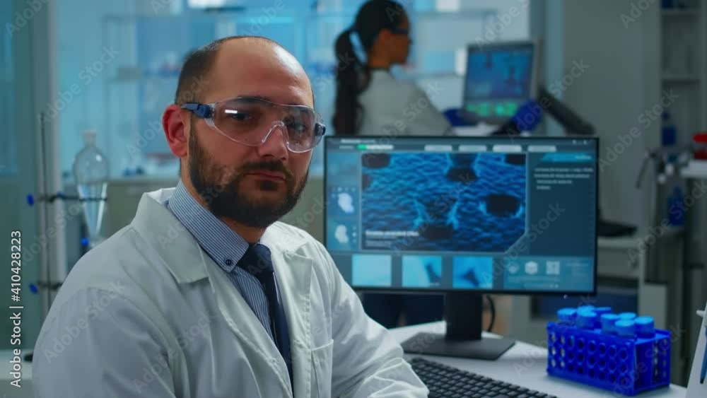 Portrait of exhausted scientist man looking at camera sitting in front of computer with DNA scan image. Chemist examining virus evolution using high tech and chemistry tools for scientific research Portrait of exhausted scientist man looking at camera sitting in front of computer with DNA scan image. Chemist examining virus evolution using high tech and chemistry tools for scientific research