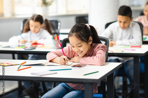 Portrait of small asian girl sitting at desk in classroom