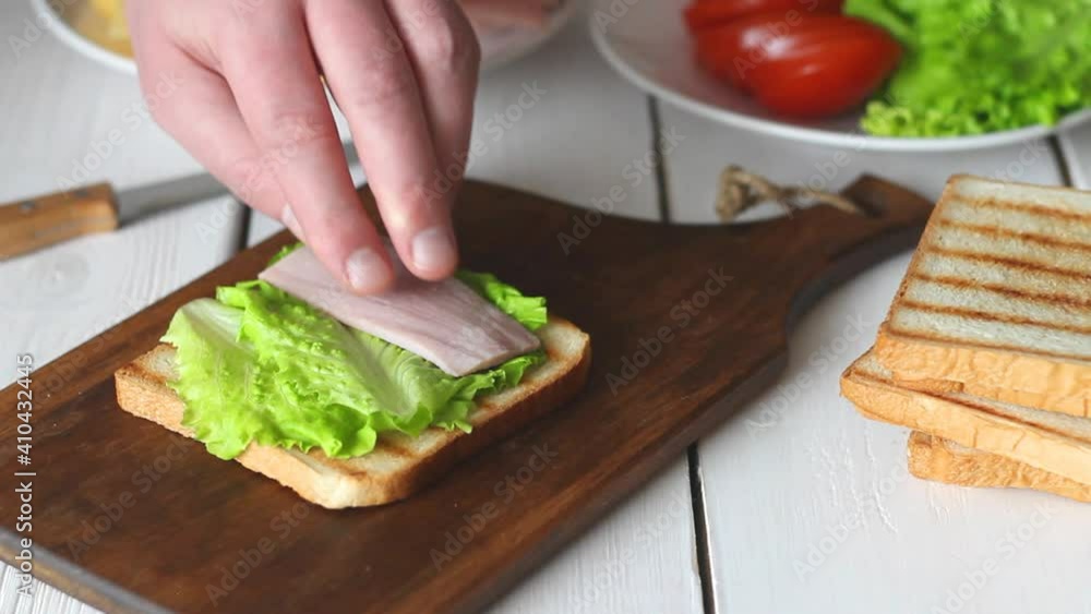 The process of making a sandwich with salad, tomato, ham and cheese. American cuisine. Fast food. Cooking. The process of making a sandwich with salad, tomato, ham and cheese. American cuisine. Fast food. Cooking.