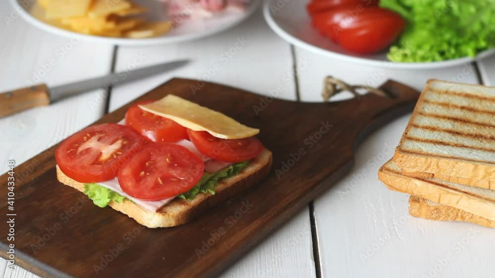 The process of making a sandwich with salad, tomato, ham and cheese. American cuisine. Fast food. Cooking. The process of making a sandwich with salad, tomato, ham and cheese. American cuisine. Fast food. Cooking.