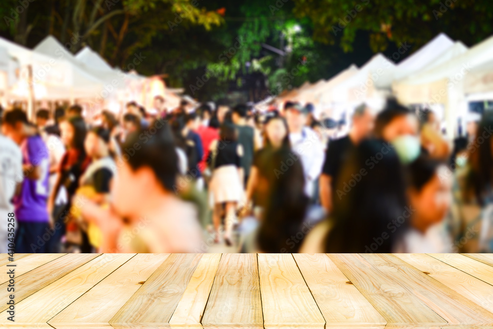 Light brown Wooden board table on front with Blurry defocused Crowd of anonymous walking shopping on night market.