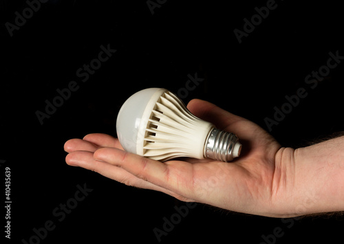 Close-up of man's hand holding energy saving light bulb on black isolated background