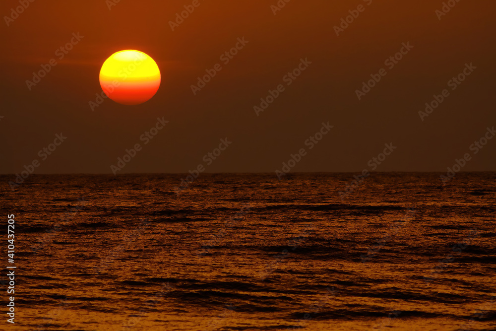 View on tropical sunset with big round sun over ocean horizon, dark shimmering water - Sri Lanka