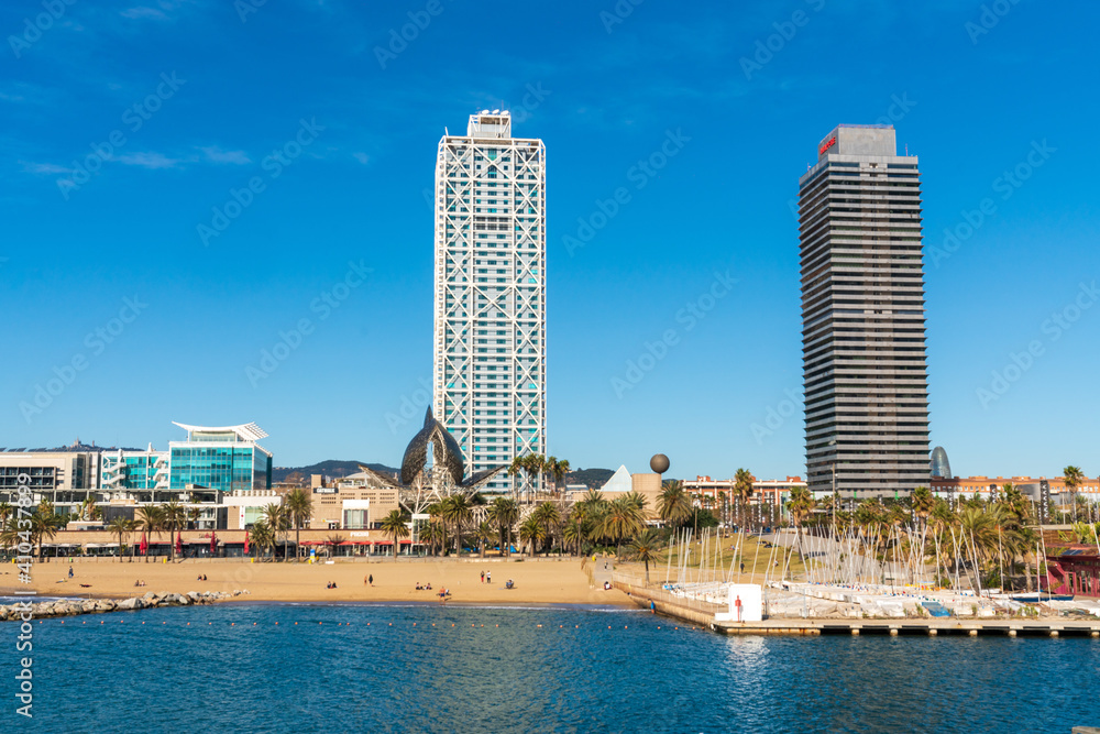 Obraz premium BARCELONA, SPAIN, FEBRUARY 3, 2021: Famous towers of the port of Barcelona, the Mapfre Tower and the Hotel Arts. Sunny winter day. During the covid-19 pandemic. Barcelona Skyline.