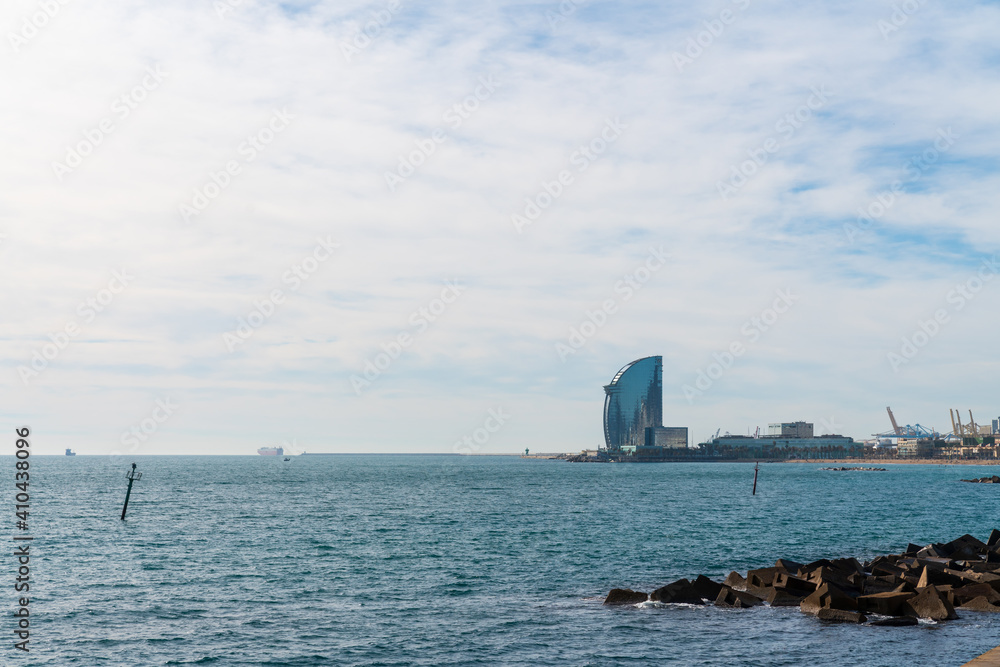 BARCELONA, SPAIN, FEBRUARY 3, 2021: The famous W hotel, known as hotel vela. Sunny winter day. View from inside the water. In the background we can see the cargo area of the port and the cable car.
