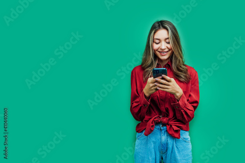 Portrait of a happy girl with a phone in her hands, she on a green background with a place for the inscription. Copy space